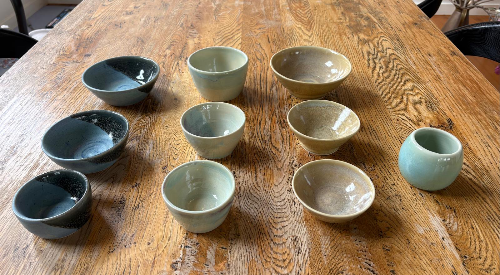 A collection of ceramic bowls in blue, sage and golden glazes on a wooden table
